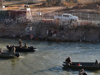 Migrants on the edge of the Rio Grande near Eagle Pass, while Texas National Guard boats pass by, on February 3.
