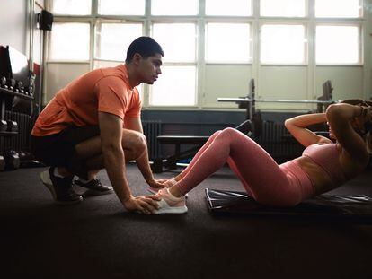 A young woman does crunches in a gym with a trainer.