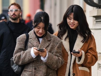 Two women walk while looking at their cell phones during Milan Fashion Week in January.