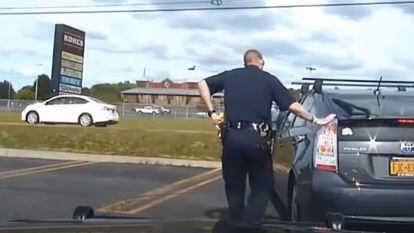 A police officer touches the back of a car after pulling it over on the highway.