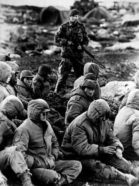 A Royal Navy officer guards Argentinean prisoners during the 1982 Falklands War.