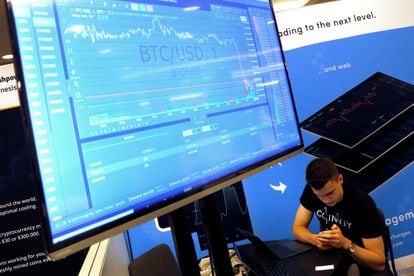 A man works beneath a display showing the market price of bitcoin.