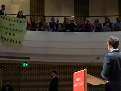 French President Emmanuel Macron looks at demonstrators unfolding a banner reading "President of Violence and Hypocrisy" in a theatre in The Hague, Netherlands, on April 11, 2023.