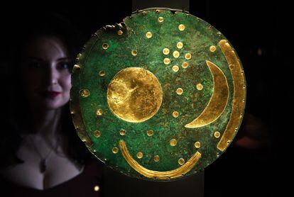 An employee at the British Museum poses next to the Nebra sky disc at the new Stonehenge exhibition.