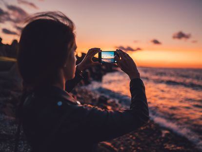 A woman uses her phone camera to capture the sunset.