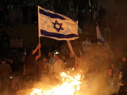 Protesters block a road and hold national flags as they gather around a bonfire during a rally against the Israeli government's judicial reform in Tel Aviv, Israel on March 27, 2023.