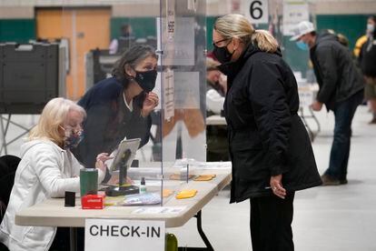 A poll worker, center left, speaks through a plastic barrier while assisting a voter in a polling station at Marshfield High School, Nov. 3, 2020, in Massachusetts.