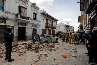 Rescue workers stand next to a car crushed by debris after an earthquake in Cuenca, Ecuador, Saturday, March 18, 2023.