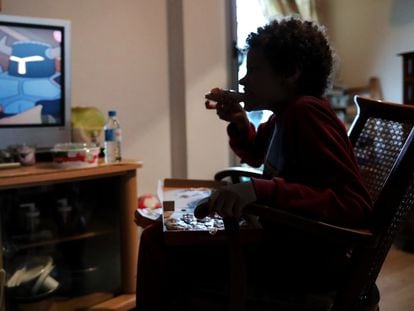 A boy eats a piece of pizza while watching television at his home in Madrid.