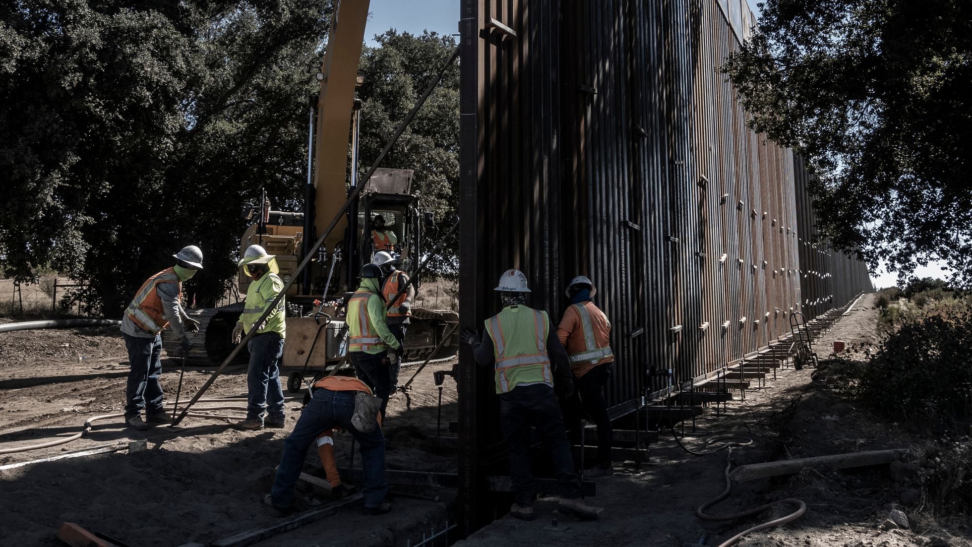 Three migrants who had managed to evade National Guard and cross the Rio  Grande onto U.S. territory wait for Border Patrol along a wall set back  from the geographical border, in El