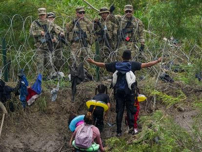 A migrant, looking to cross to the U.S., holds out his arms while appealing to Texas National Guardsmen standing behind razor wire on the bank of the Rio Grande, on May 11, 2023.