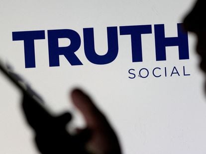 The Truth social network logo is seen displayed behind a woman holding a smartphone.