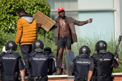 A seasonal worker in Albacete faces police with a sign reading: “Please, please, we need our release to leave. We have a family.”