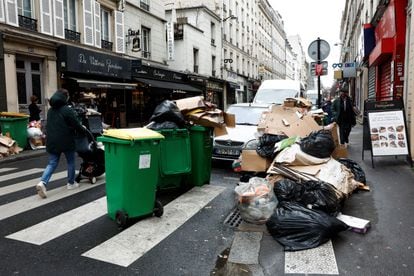 People walk in a street where garbage cans are overflowing, as garbage has not been collected, in Paris, France March 13, 2023. 