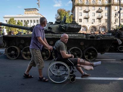 A man pushes a Ukrainian serviceman's wheelchair past a destroyed Russian tank on display in central Kyiv during Independence Day celebrations on August 24, 2023.