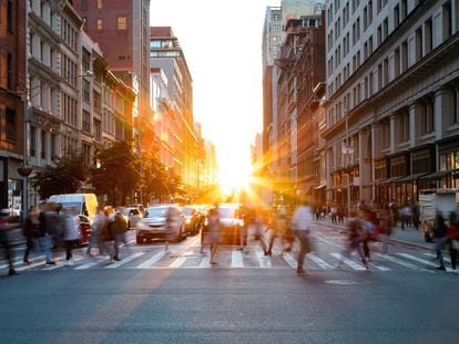 Crowds of busy people walking through the intersection of 5th Avenue and 23rd Street in Manhattan, New York City with bright sunset background.