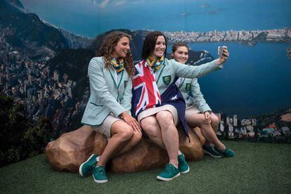 Australians pose for a selfie in front of an image of the Olympic Village.