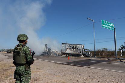 A soldier stands guard before the remains of a burned-out vehicle in Mazatlán (Sinaloa).