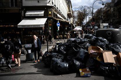 Pedestrians walk past a pile of garbage bags that have been piling up since waste collectors went on strike against the French government's proposed pensions reform, in Paris on March 15, 2023. 