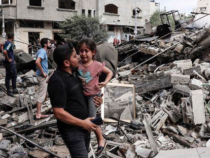 A man carries a crying child as he walks in front of a building destroyed in an Israeli air strike in Gaza City on October 7, 2023.