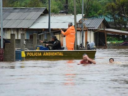 Police officers check a house as residents wade through a flooded street after floods caused by a cyclone in Passo Fundo, Rio Grande do Sul state, Brazil