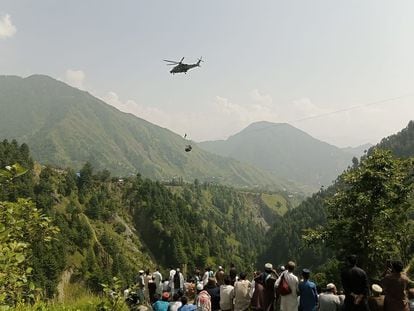 People watch as an army soldier slings down from a helicopter during a rescue mission to recover students stuck in a chairlift in Pashto village of mountainous Khyber Pakhtunkhwa province, on Aug. 22, 2023.