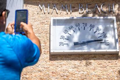 A person takes a photo of a Miami Beach Clock Thermometer that marks the temperature at 105 degrees Fahrenheit