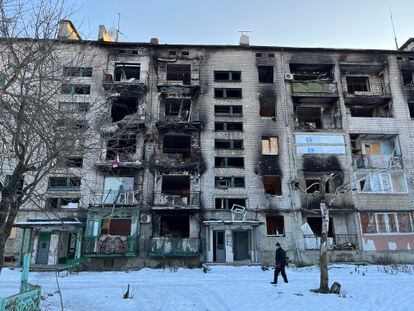 A resident of Lyman, in the Donetsk region, walks through the snow in front of a shelled building.
