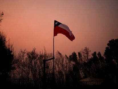 A Chilean flag stands amid charred trees under a red sky caused by wildfires in Santa Juana, Chile