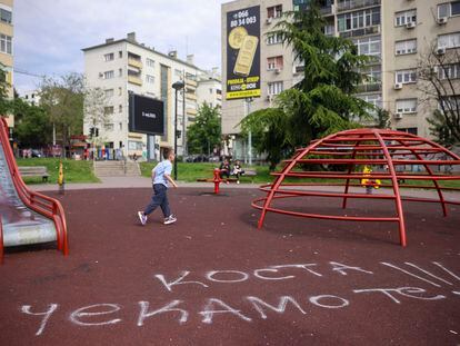 A boy walks past graffiti on a playground that reads "Kosta we are waiting for you," in Belgrade, Serbia, on May 6, 2023.