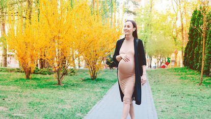 A pregnant woman walks through a park.