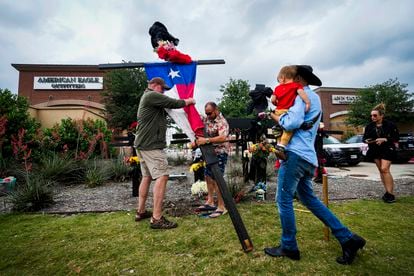 Residents raise a cross with a Texas flag as they construct a memorial outside an entrance to the mall a day after a mass shooting at Allen Premium Outlets on May 7, 2023, in Allen, Texas.