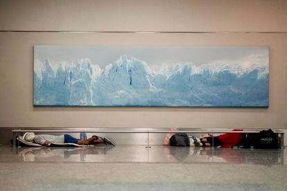 Homeless men sleep below a photo of the Perito Moreno Glacier at the Jorge Newbery international airport, commonly known as Aeroparque, in Buenos Aires, Argentina