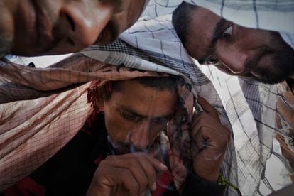Varios hombres consumed droga protegidos por un pañuelo en el cauce del río Kabul.  A pocos metros, un pequeño túmulo de tierra marca el lugar donde ha sido enterrado un par de días antes un hombre que murió en este mismo lugar. 