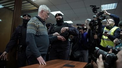 A police officer places handcuffs on Memorial activist Oleg Orlov during a court hearing in Moscow on February 27.