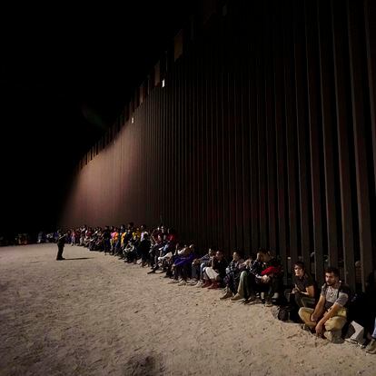 Migrants wait along the border wall after crossing from Mexico to the US near Yuma (Arizona).