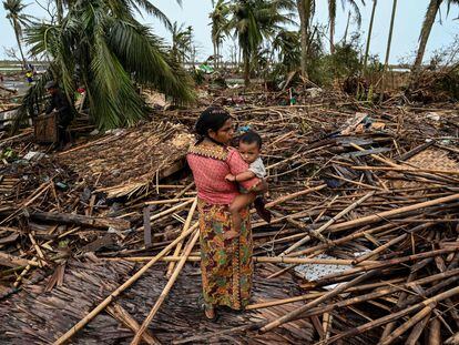 A Rohingya woman carries her baby next to her destroyed house at Basara refugee camp in Sittwe on May 16, 2023, after Cyclone Mocha made a landfall.
