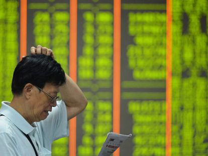 An investor reads in front of a board of share prices in China. Falls are shown in green.