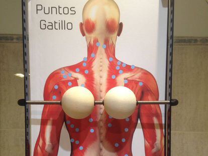 The massage device consists of two wooden balls held in place by a metal rod that is attached to a frame.