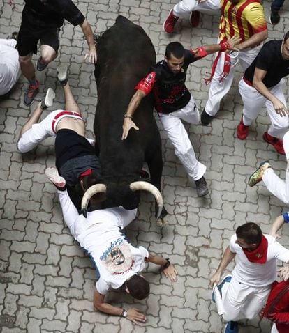 A bull charges over a runner in the underpass leading to the bullring.