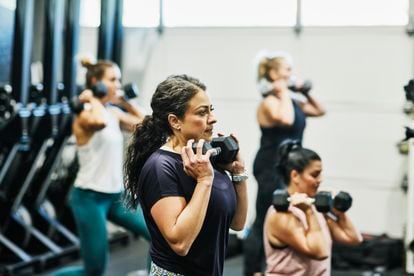 Woman doing dumbbell squats during fitness class in gym.