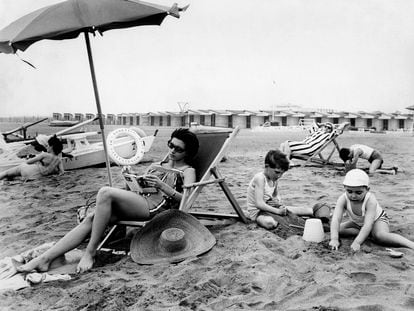 A woman reads on the beach under an umbrella, in 1962.