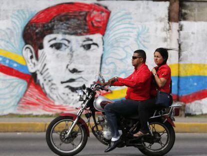 A couple rides past a street mural of Hugo Ch&aacute;vez in the city of Barinas.