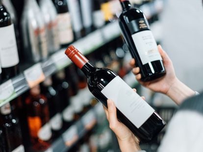 A woman chooses bottles of red wine from the shelf in a supermarket.