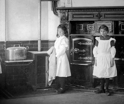 Two girls pose in the kitchen of the house where they worked as maids, in an image dated to the Victorian era.