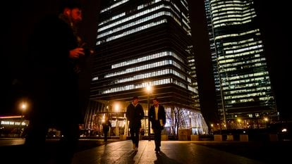 Two young people walk in front of the area of the four business towers in Madrid, Spain.