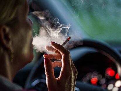 A woman smokes a cigarette inside a car