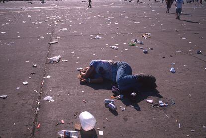 A Woodstock ’99 festivalgoer sleeps in the sun on a concourse littered with garbage.