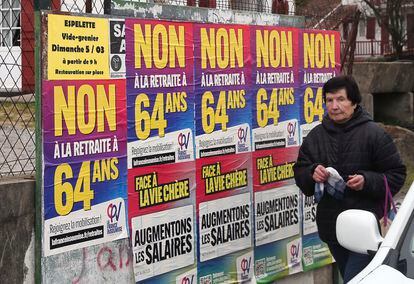 A woman walks past "No retirement at 64" posters in Saint Pee sur Nivelle, southwestern France, on Monday, March 6, 2023.