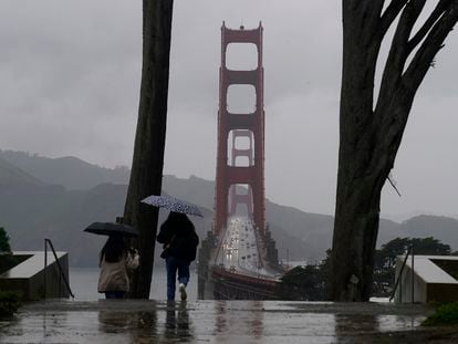 Traffic moves on the Golden Gate Bridge as people carry umbrellas while walking down a path at the Golden Gate Overlook in San Francisco, March 9, 2023.